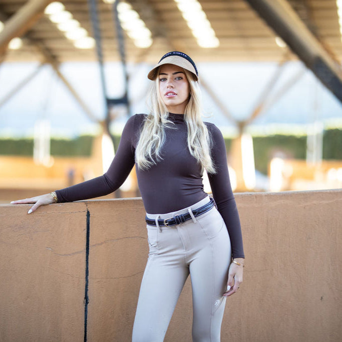Woman in equestrian attire standing in an indoor arena.